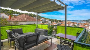 Un balcon avec une table et des chaises, une clôture verte et une vue sur la ville et la mer.