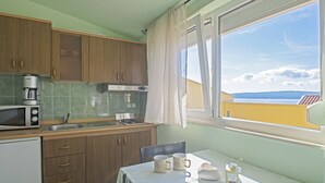 A compact kitchen with wooden cabinets, a microwave, and a window with a view of a distant landscape. - Apartments Oaza (Dramalj)