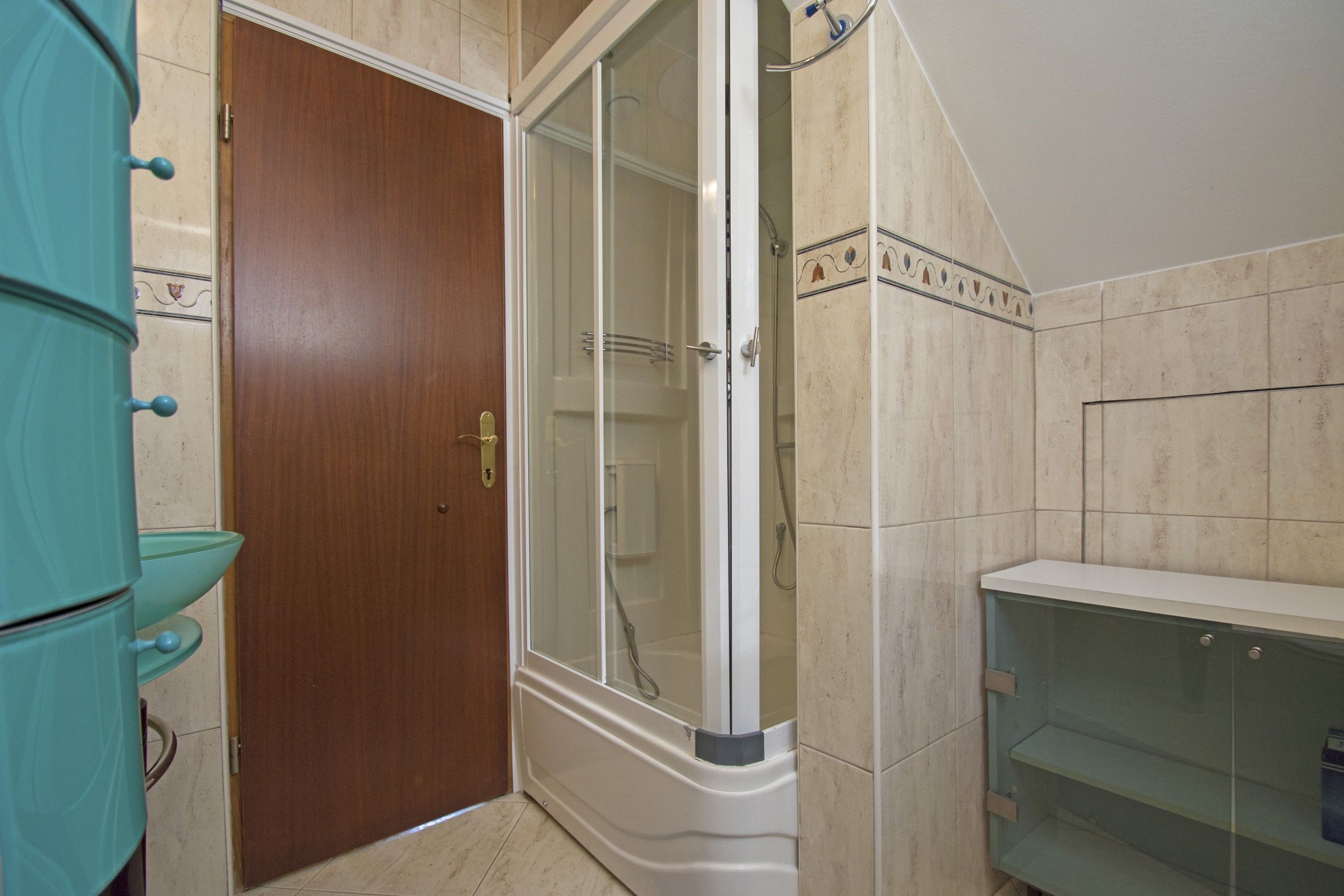 A bathroom with a wooden door, a glass shower enclosure, and a glass shelf unit.