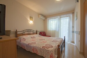 A bedroom with a bed, a bedside table, a chair, a wall-mounted air conditioner, and a window with curtains.