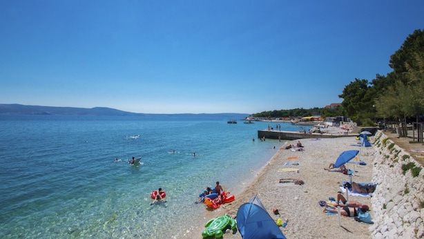 A beach with clear water, people swimming and sunbathing, and a rocky shoreline. - Apartments Franny (Novi Vinodolski)