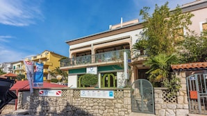A two-story building with a stone wall, a balcony with metal railings, and a sign indicating it is a hotel. - Apartment Riky (Crikvenica)