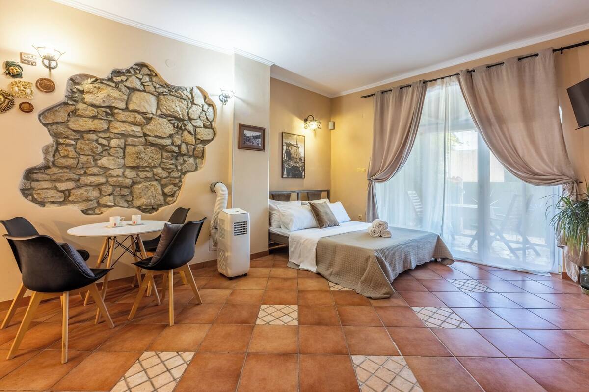 Een hotelkamer met een stenen muur, een bed, een zithoek met stoelen en een groot raam met gordijnen.