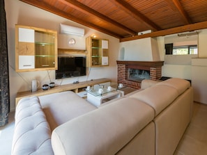 Un soggiorno moderno con un ampio divano beige, un soffitto in legno, un caminetto in mattoni e una televisione a schermo piatto montata a parete.