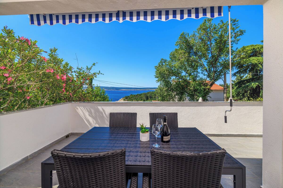 A patio with a table and chairs, a bottle of wine, and a glass of water.