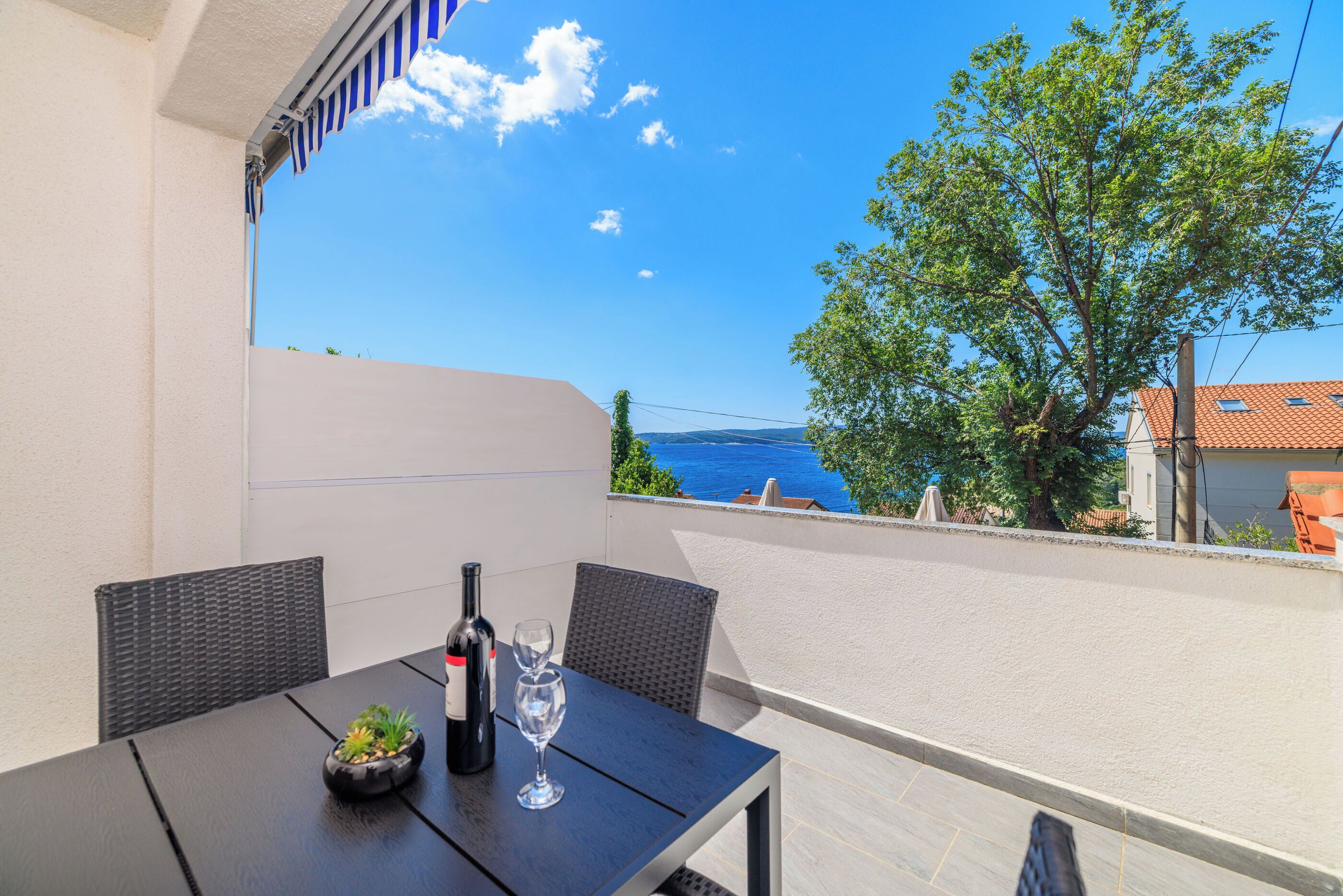 Een balkon met een tafel, stoelen, een fles wijn en een glas.