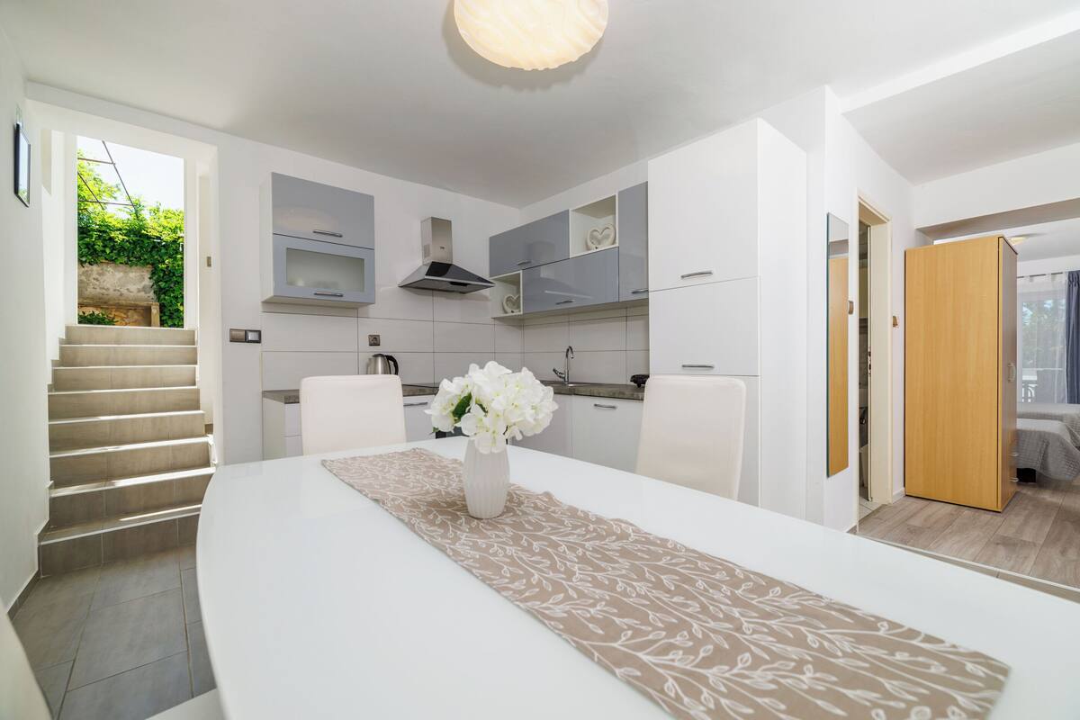 A modern kitchen with white cabinets, a built-in stove, and a dining area with a white table and a decorative runner.
