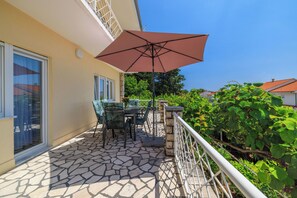 A patio with a table and chairs, a large umbrella, and a stone-tiled floor. - Apartment Andelko (Dramalj)