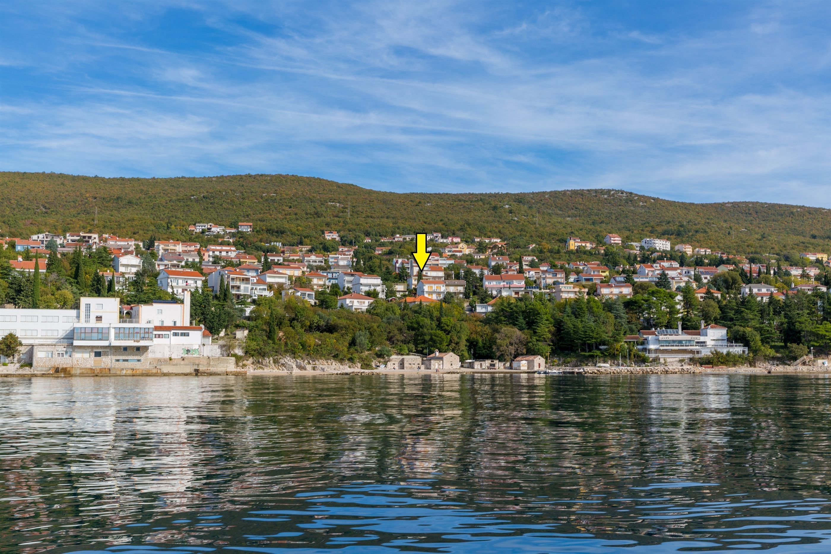 A coastal town with buildings along the waterfront, a hill in the background, and a body of water in the foreground.