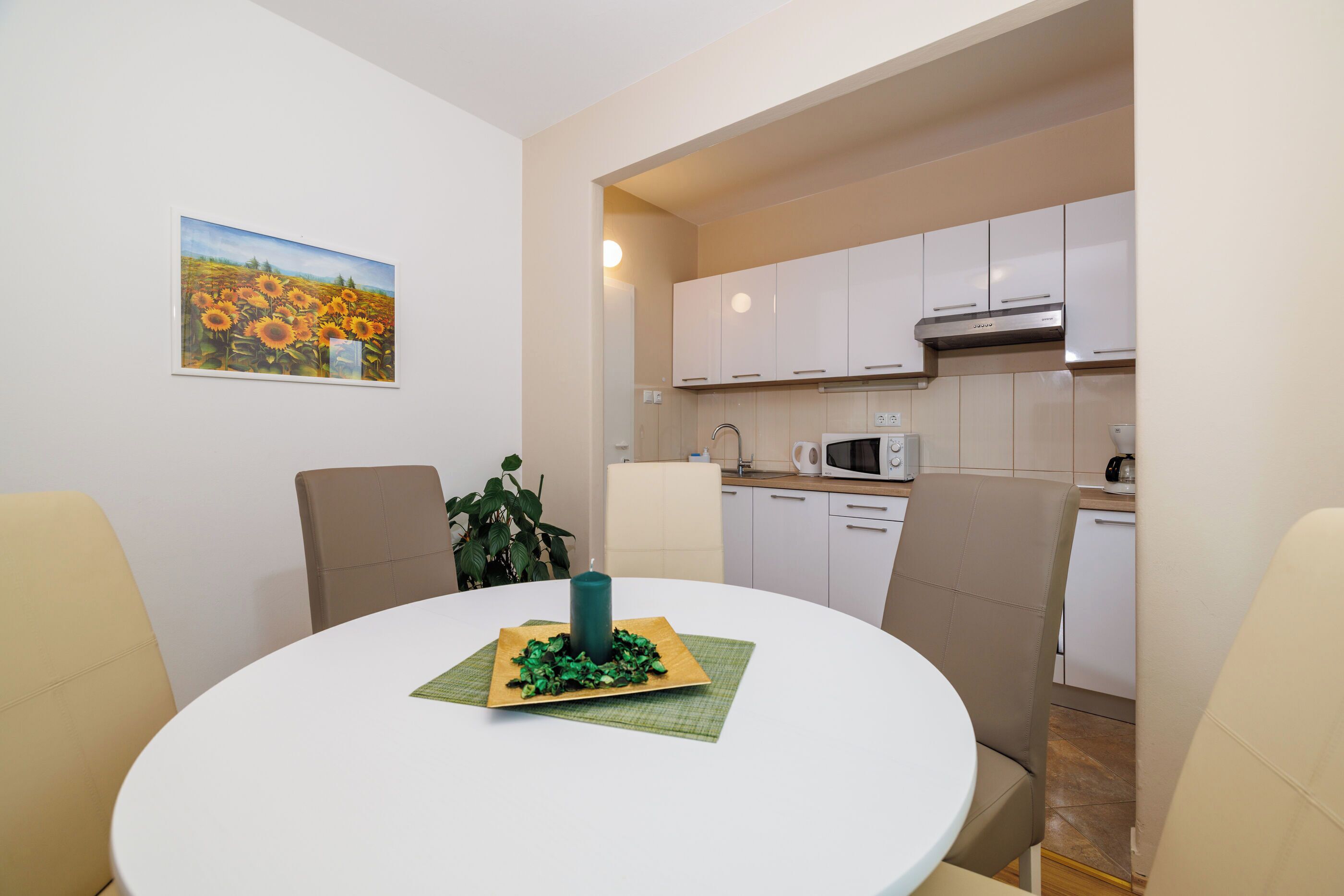 Un coin repas avec une table ronde, des chaises, un centre de table à bougie et un tableau représentant un tournesol accroché au mur.