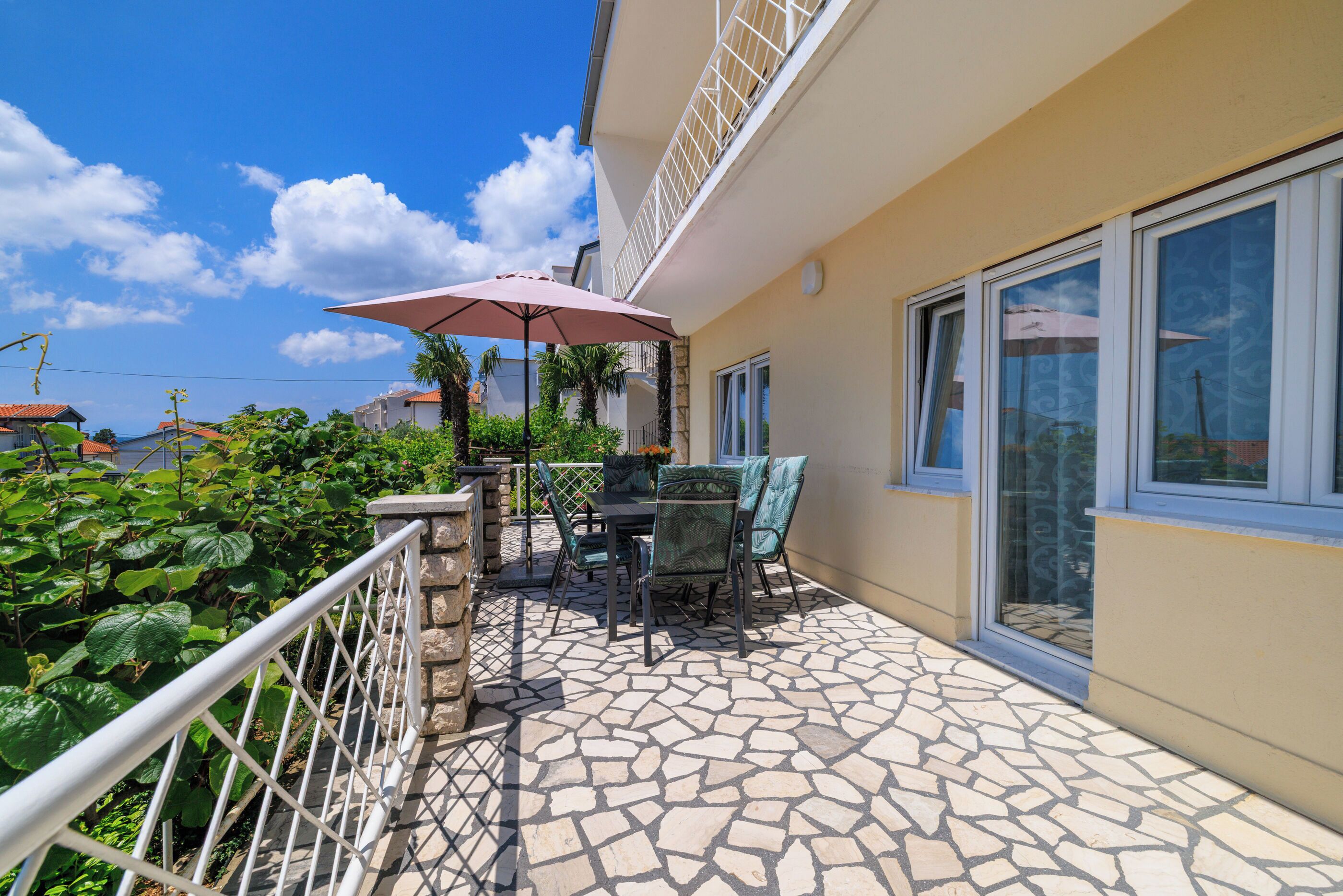 Un balcon avec un sol carrelé en pierre, une table avec des chaises et un parasol de patio.