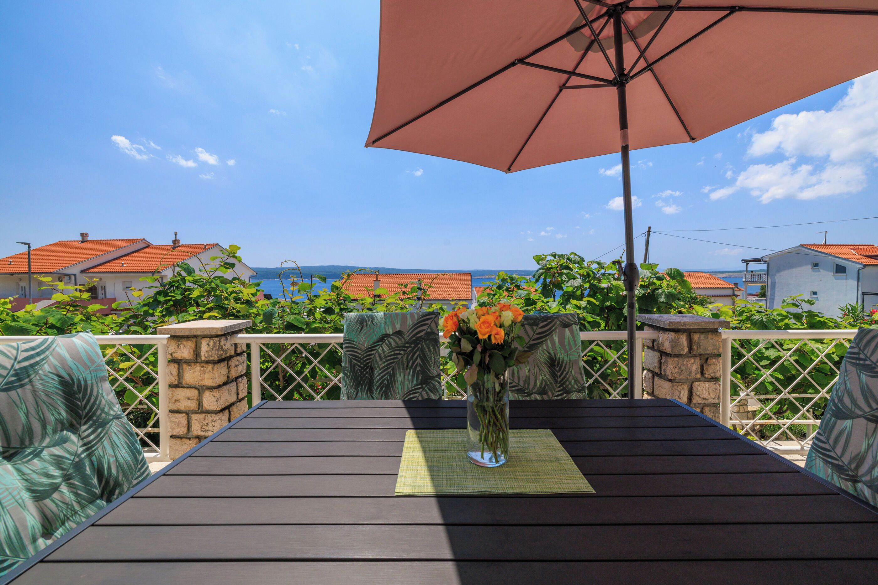 Une terrasse en bois avec une table, un vase rempli de fleurs et un grand parasol.
