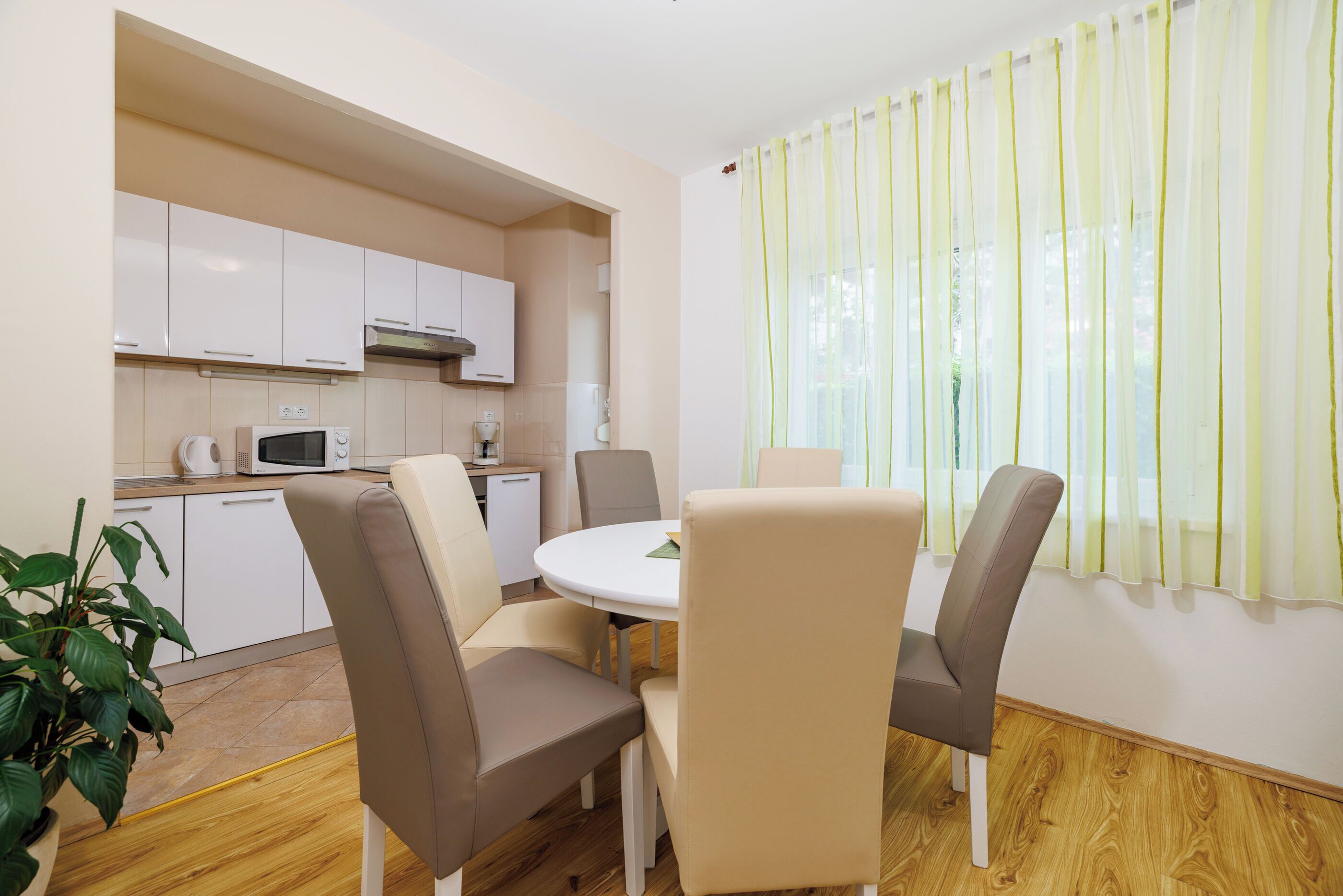 A modern kitchen with white cabinets, a microwave, and a coffee machine. There is a dining area with a round table and four chairs.