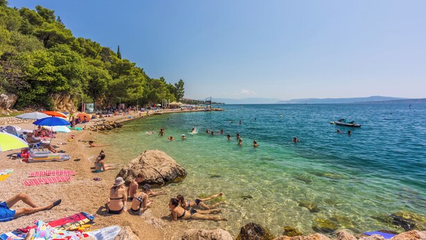 Egy tiszta vizű strand, ahol az emberek úsznak és napoznak, és napernyők is találhatók.