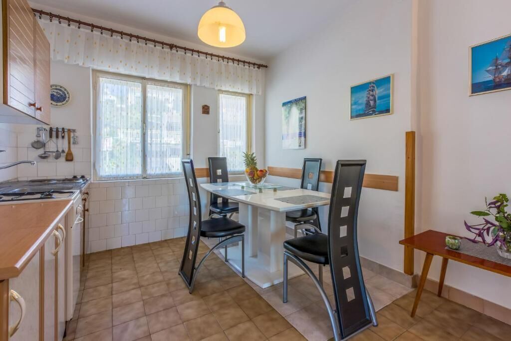 A kitchen with a dining table, chairs, a hanging light fixture, and a window with curtains.