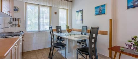 A kitchen with a dining table, chairs, a hanging light fixture, and a window with curtains.