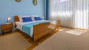 Ein Schlafzimmer mit einem Bett, Nachttischen und einem großen Fenster mit transparenten Vorhängen.