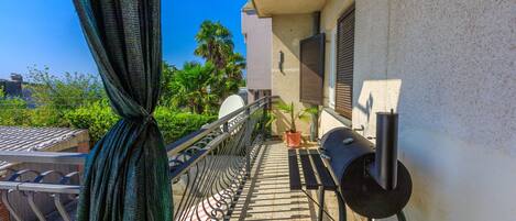 Un balcon agrémenté d’un barbecue, de plantes en pot et offrant une vue sur la verdure environnante.