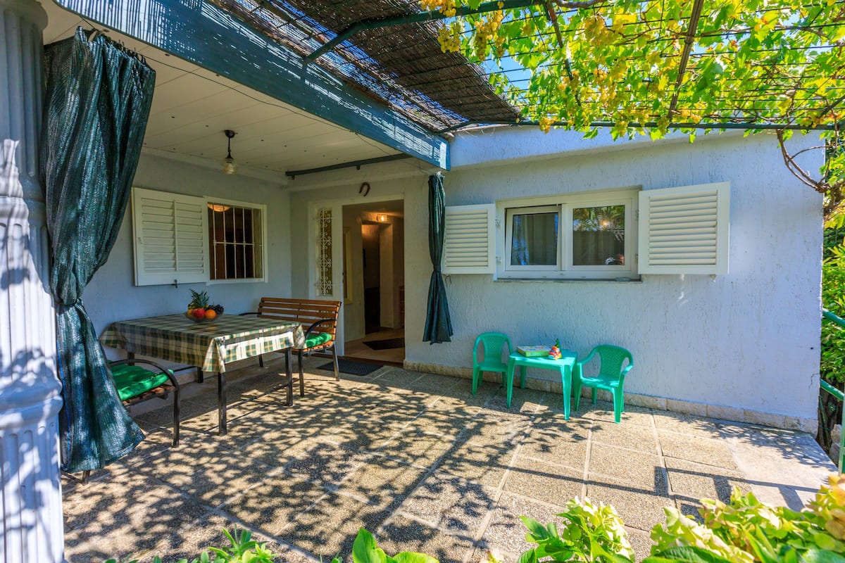 Une terrasse couverte avec une table et des chaises, un banc et une petite table sur laquelle se trouve un panier de fruits.