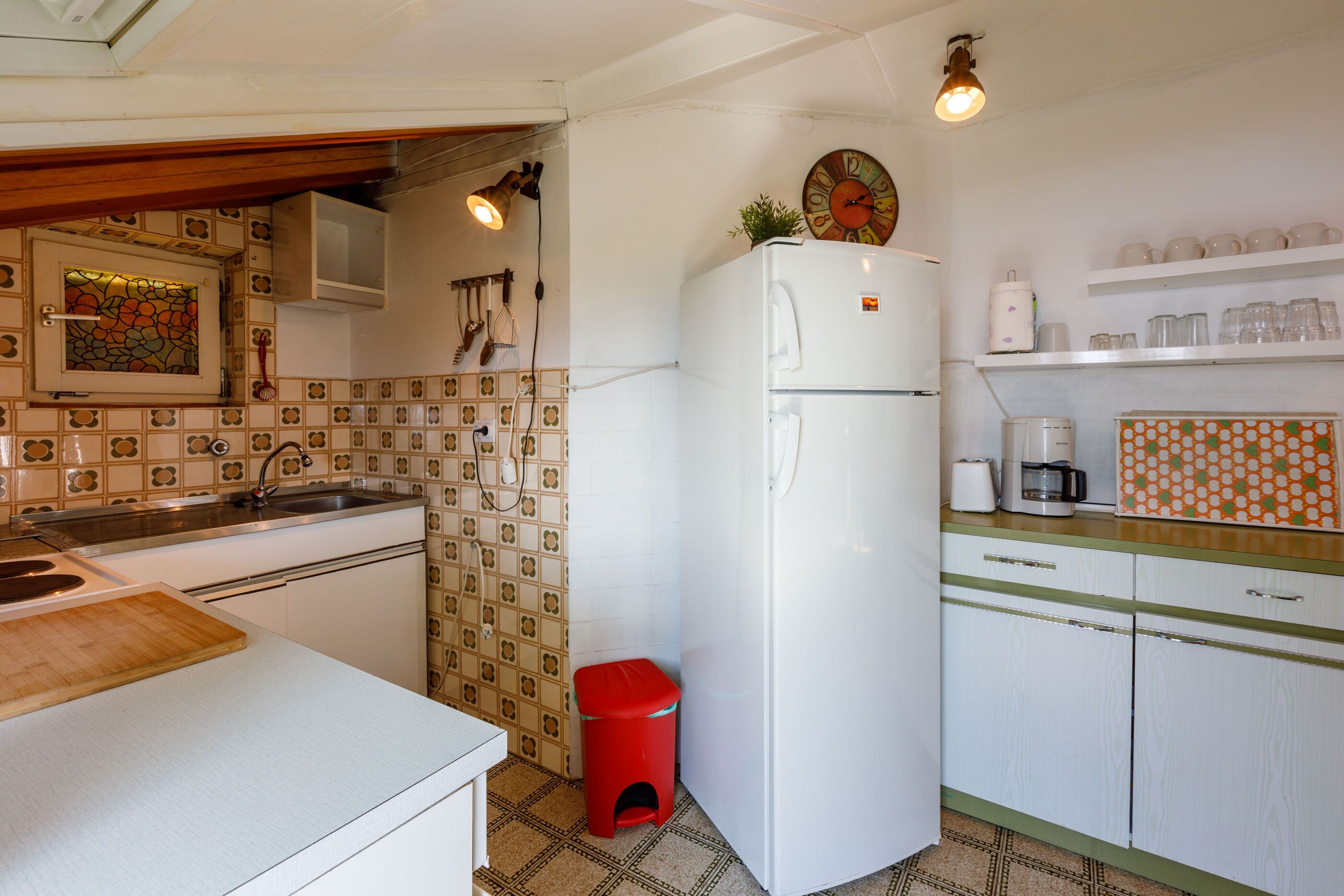 Eine kleine Küche mit Kühlschrank, Spüle und einem kleinen Hocker.