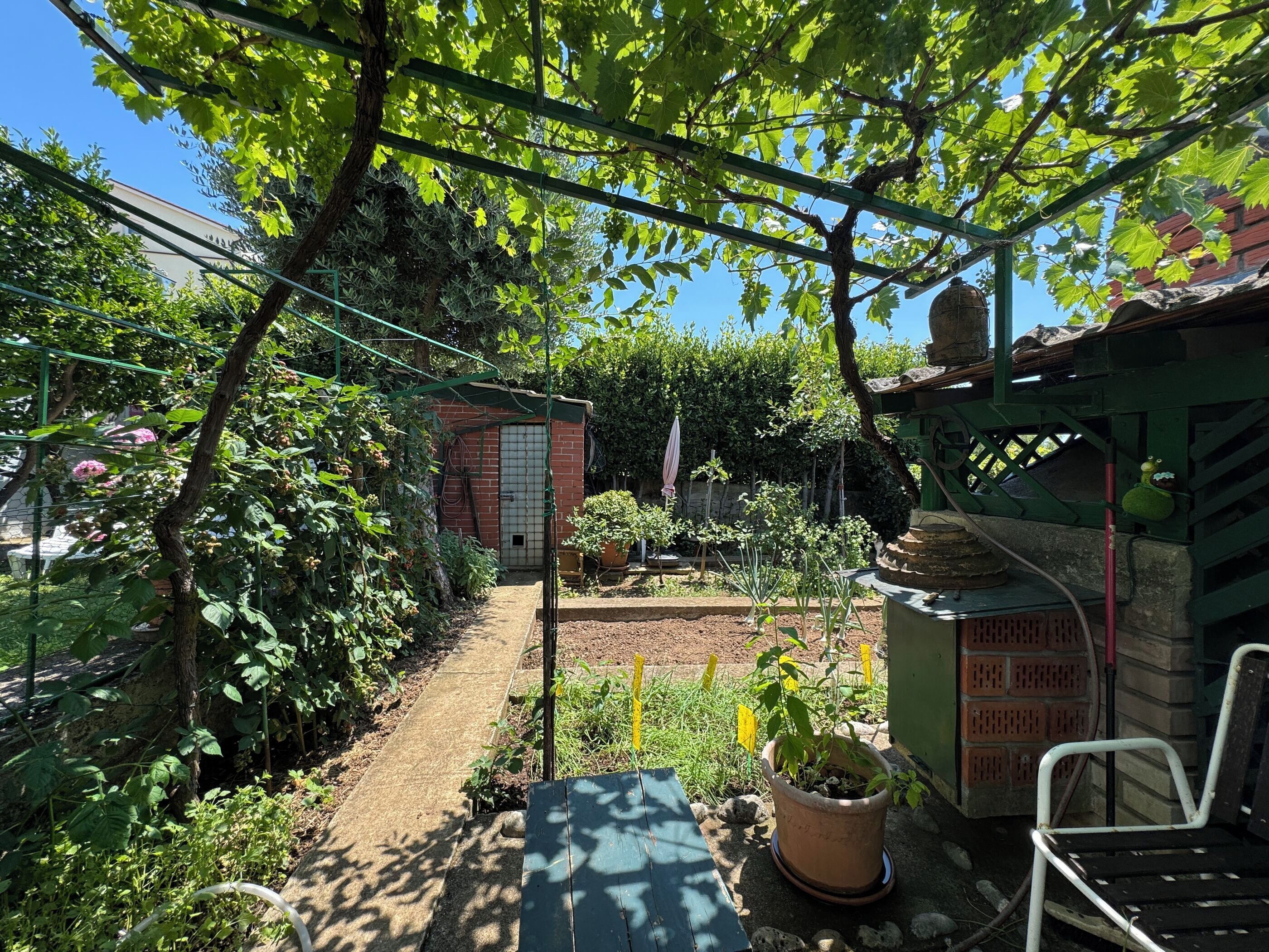 A garden with a brick structure, potted plants, and a wooden bench.