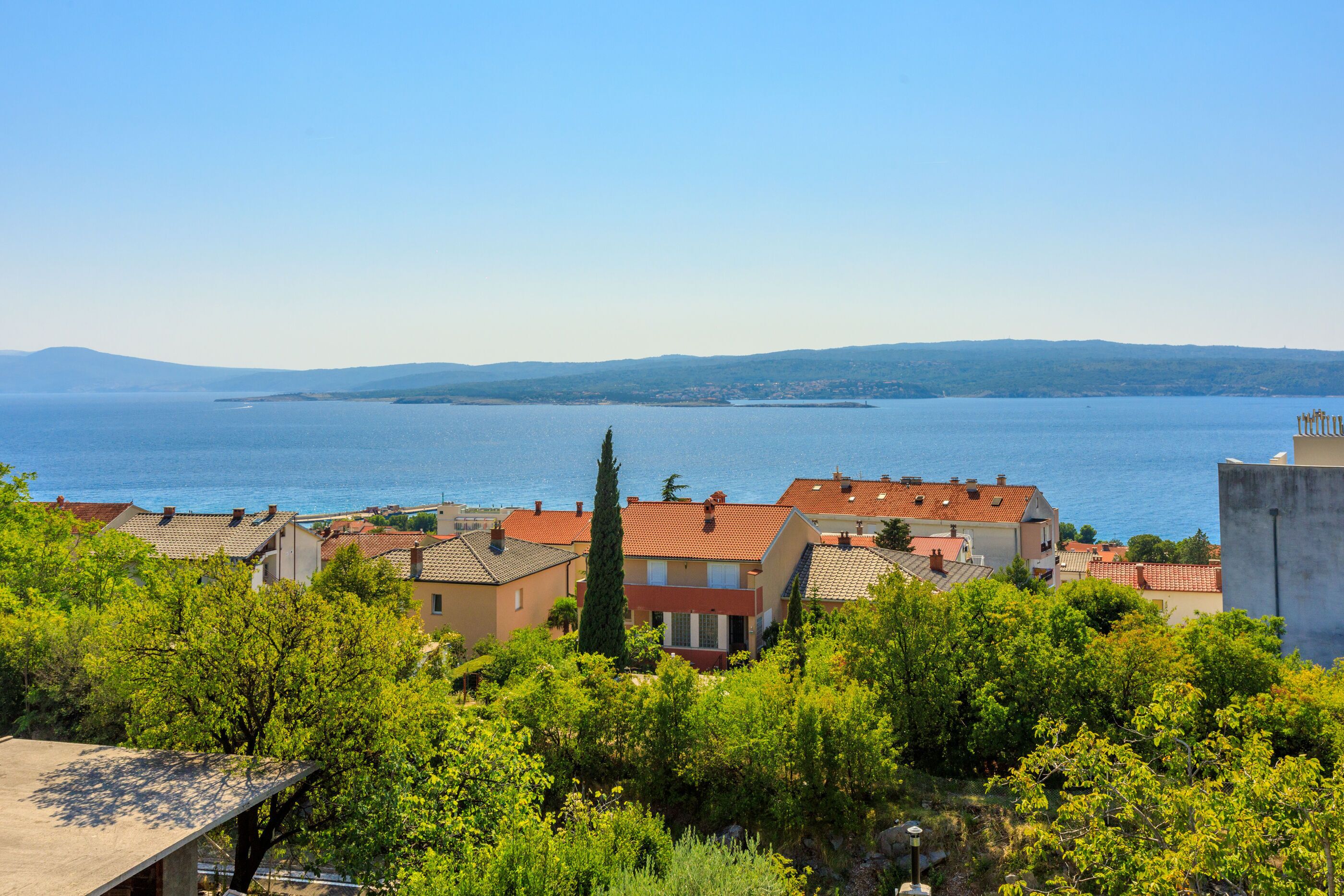Eine Küstenstadt mit Häusern, freiem Blick auf das Meer und einer fernen Bergkette.