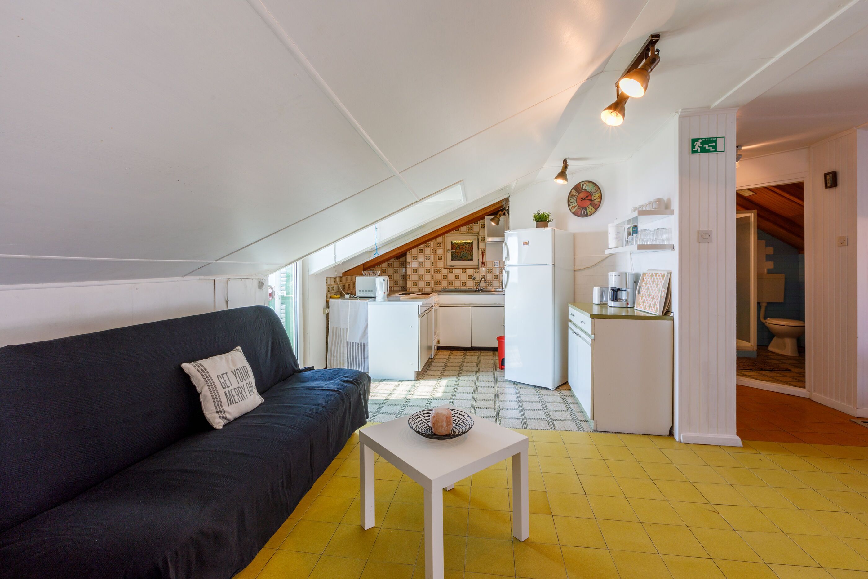 A compact living space with a sofa, a small table, and a kitchenette in the background.