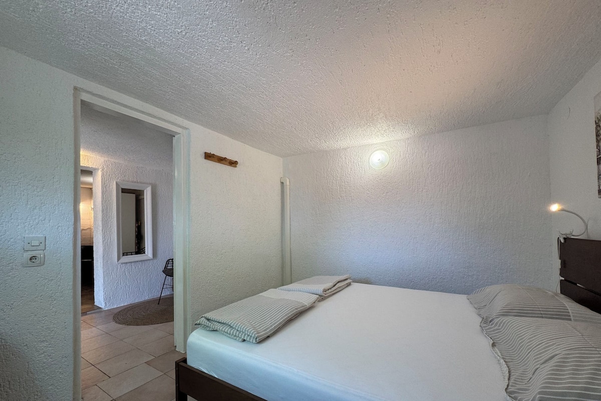 Une chambre à coucher comprenant un lit, une table de chevet, une lampe fixée au mur et une porte donnant sur une autre pièce.