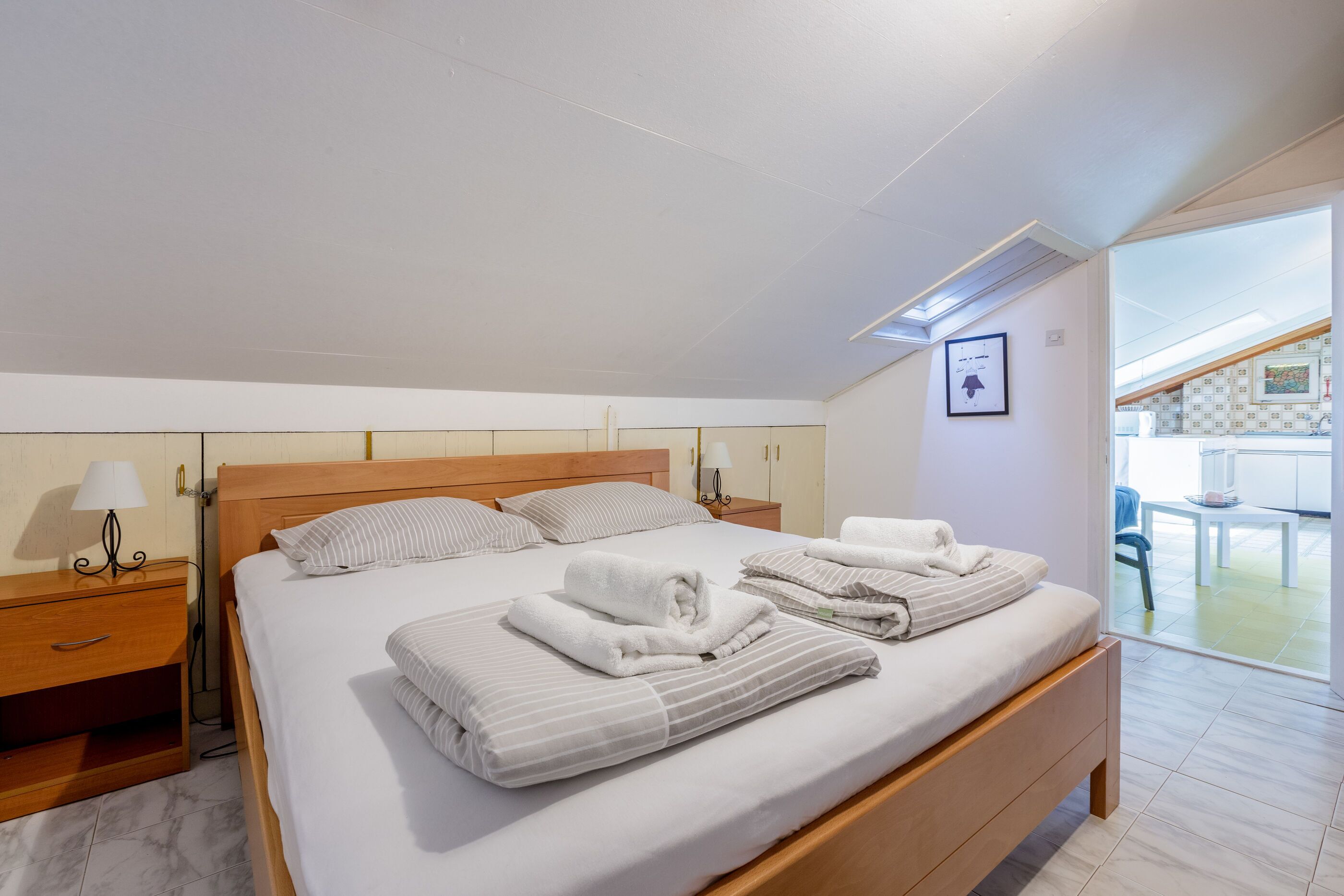 A modern hotel room with a large bed, wooden headboard, and a view of the outdoor area through a glass door.