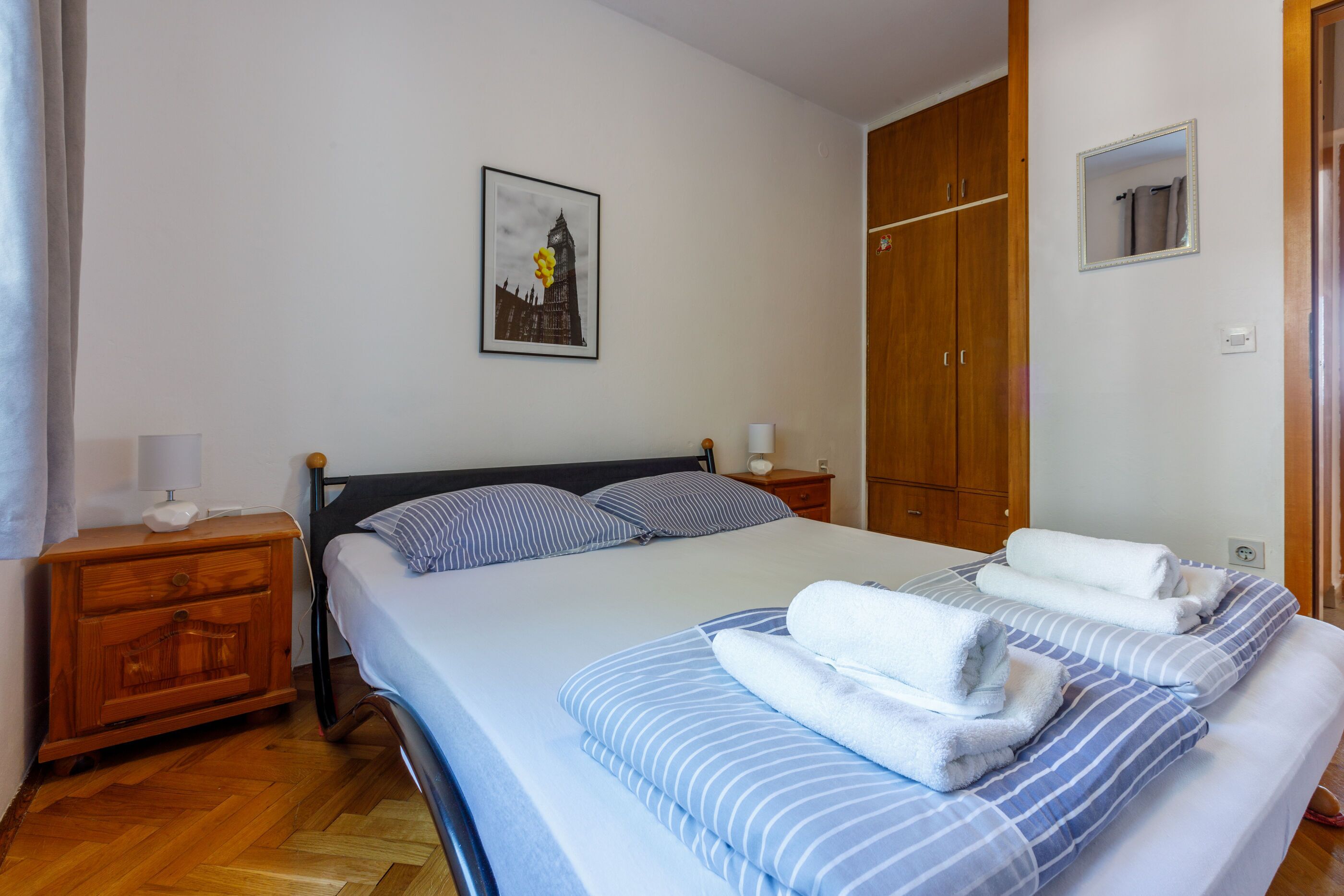 Ein Schlafzimmer mit einem Bett, einem Holzschrank, einem Nachttisch und einem gerahmten Bild an der Wand.