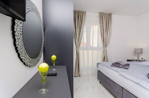 Une chambre d’hôtel moderne, dotée d’un grand miroir, d’une table de chevet avec une lampe, d’un lit avec une couverture soigneusement disposée et d’une fenêtre avec des rideaux.
