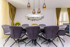 Un espace de salle à manger moderne avec une table ronde, des chaises violettes et des luminaires suspendus.
