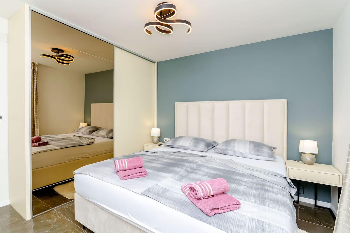A modern bedroom with a large bed, two bedside tables with lamps, and a mirror on the wall.