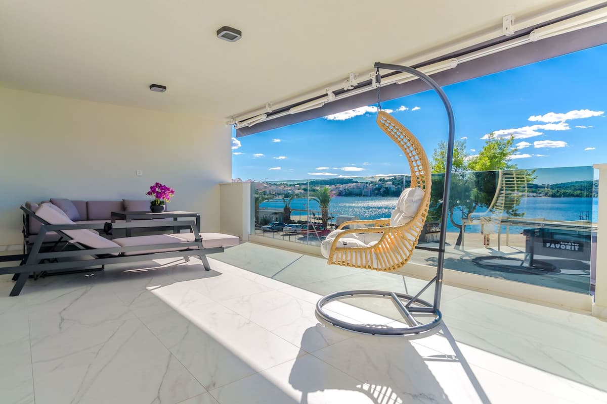 A balcony with a hanging chair, a sofa, and a view of a body of water and distant landscape.