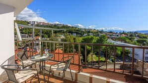 A balcony with a table and chairs, offering a view of a hillside town and a bridge. - Apartments Franka (Crikvenica)