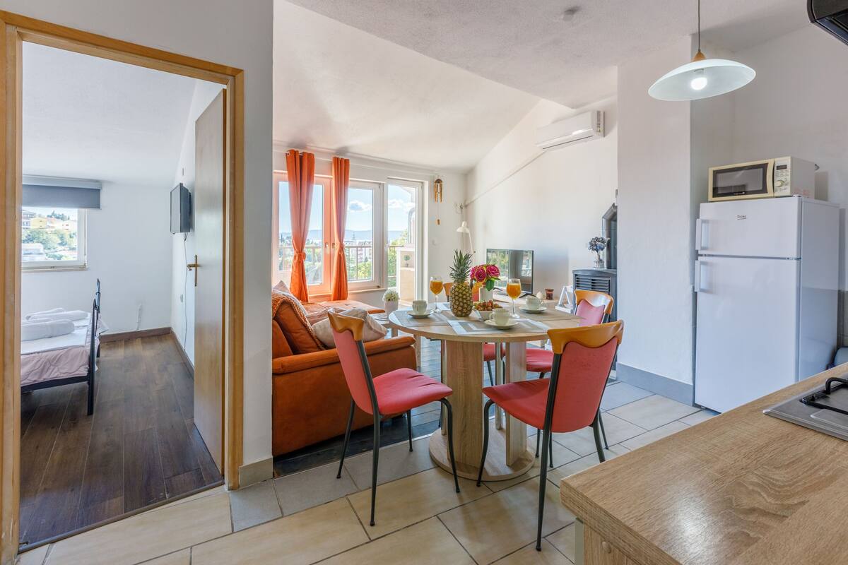 A modern kitchen with a dining area, featuring a round table with chairs, a refrigerator, and a microwave.