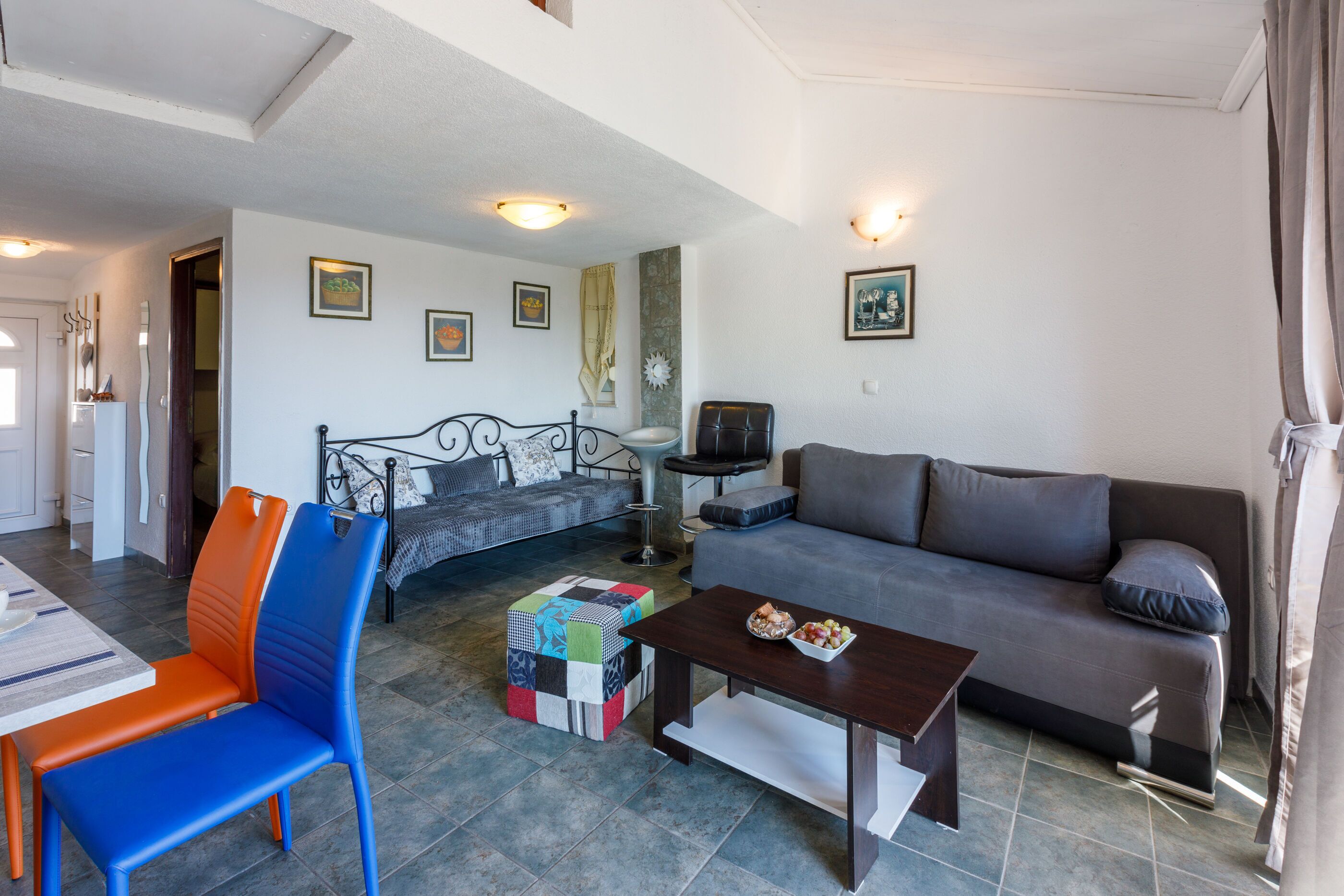 A living room with a sofa, a coffee table, a TV, and a colorful ottoman.