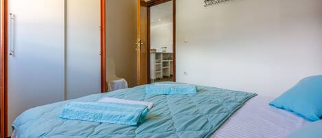 Un dormitorio con cama, dos almohadas, colcha azul y armario de madera.