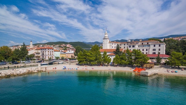 A coastal town with a prominent white building with a tower, a sandy beach, and a calm sea. - Apartments Franka (Crikvenica)