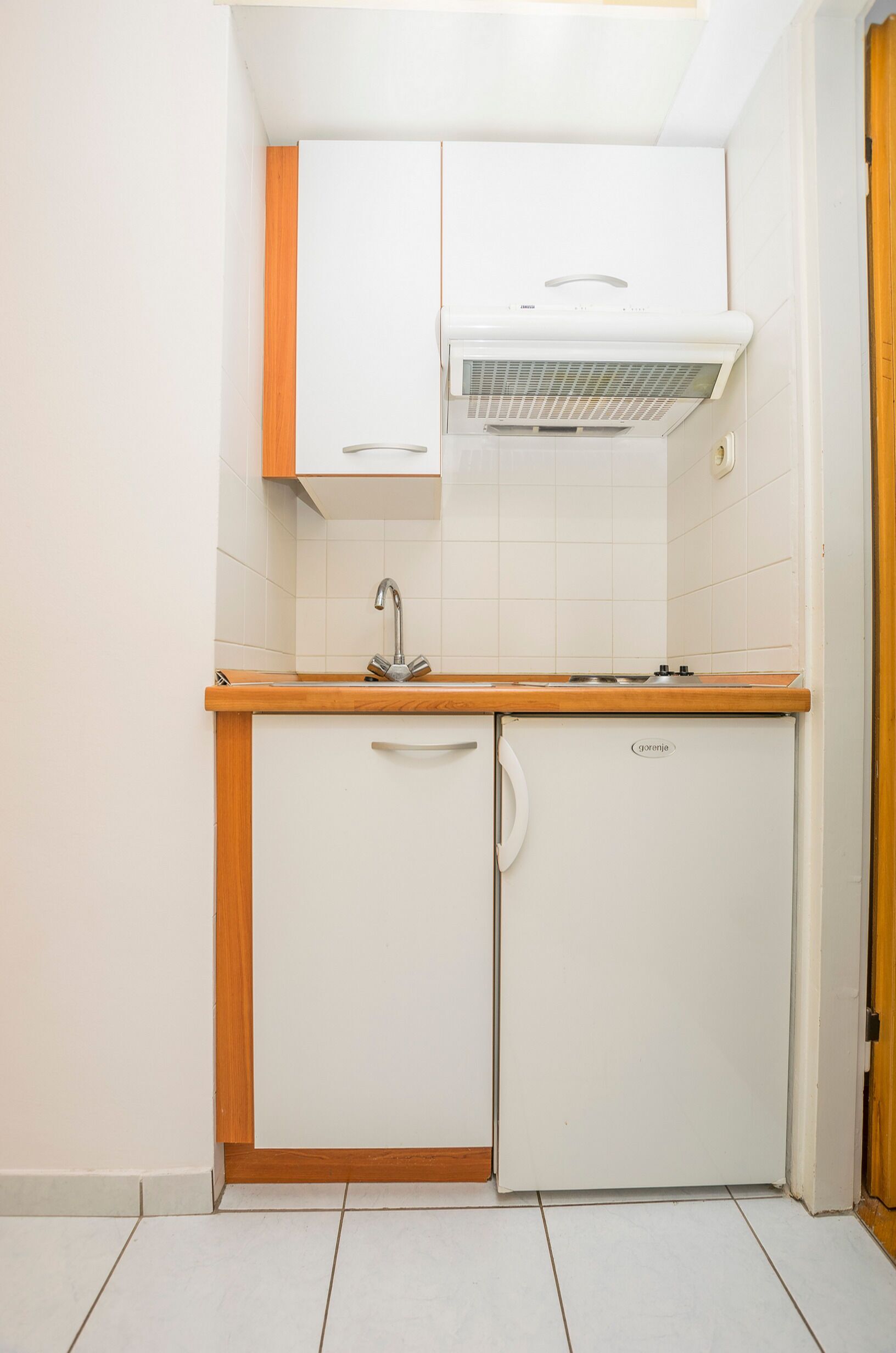 Una cocina compacta con armarios blancos, horno integrado y un lavamanos.