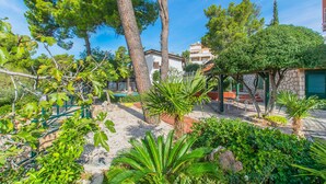Un jardin avec différentes plantes et arbres, un bâtiment en pierre et une maison blanche avec un toit rouge.