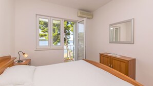 Une chambre à coucher comprenant un lit, une table de chevet, une commode, une fenêtre donnant sur des arbres et un appareil de climatisation.