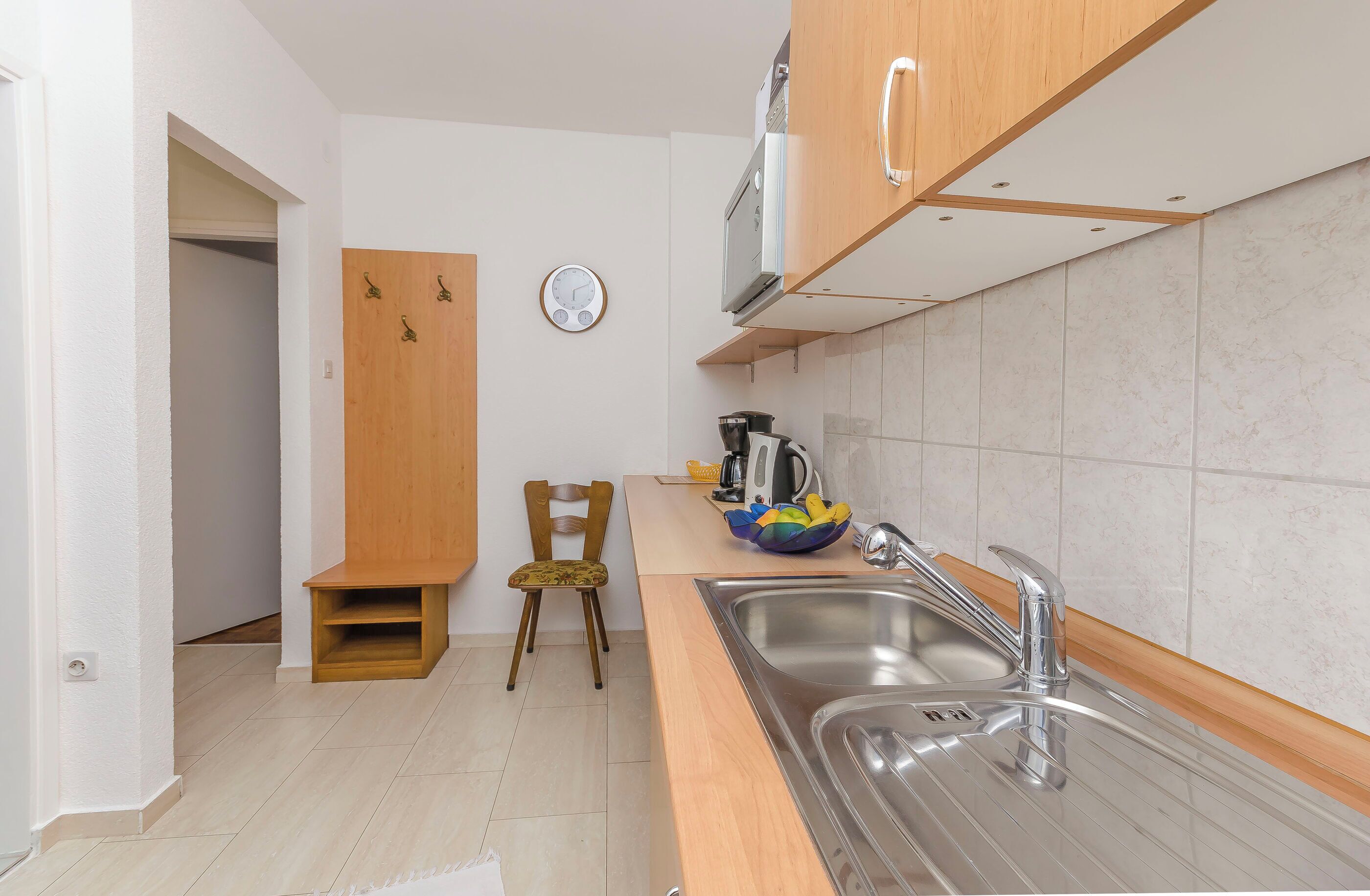 Una cocina moderna con un lavamanos, armarios de madera, un reloj y una silla.