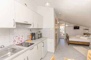Eine moderne Küche mit weißen Schränken, einem Spülbecken und einer Mikrowelle. Auf der Arbeitsfläche steht ein kleiner Kühlschrank und eine Kaffeemaschine.