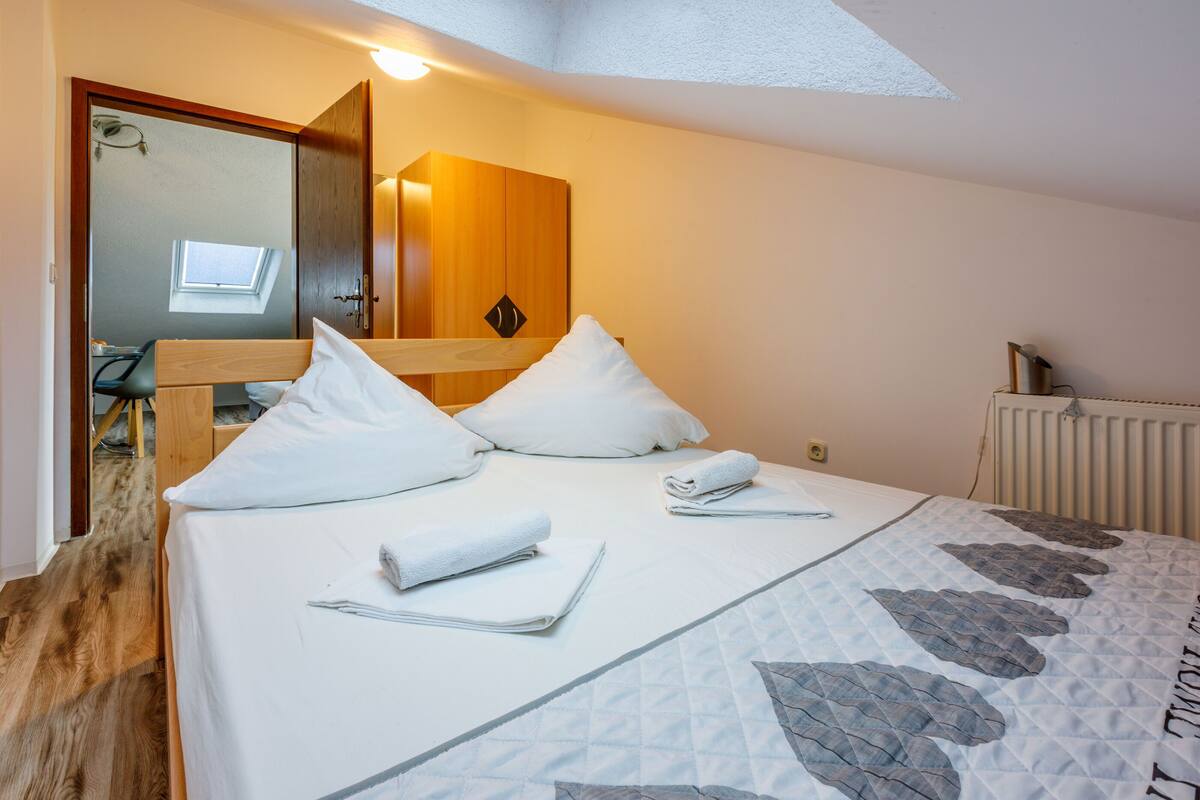 Un lit bien fait, avec du linge de lit blanc et une couverture matelassée, une tête de lit en bois et une lucarne au-dessus.