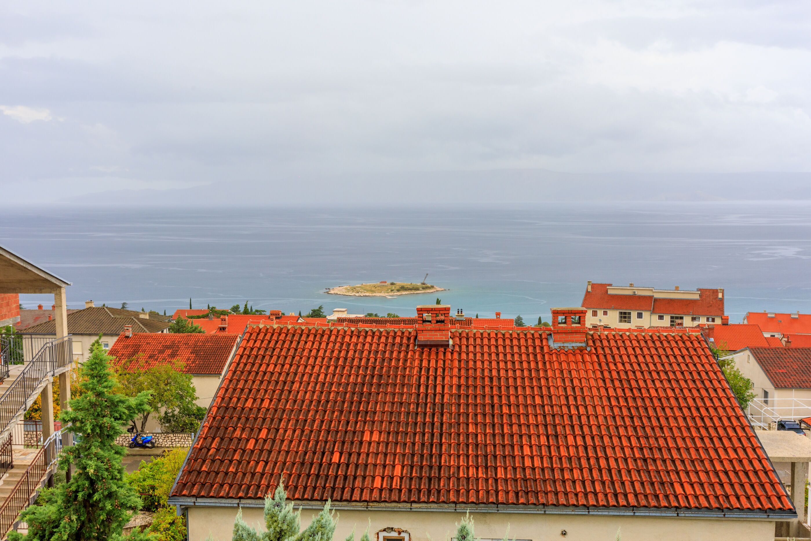 A coastal residential area with red-tiled roofs, a small island in the distance, and a clear view of the sea.