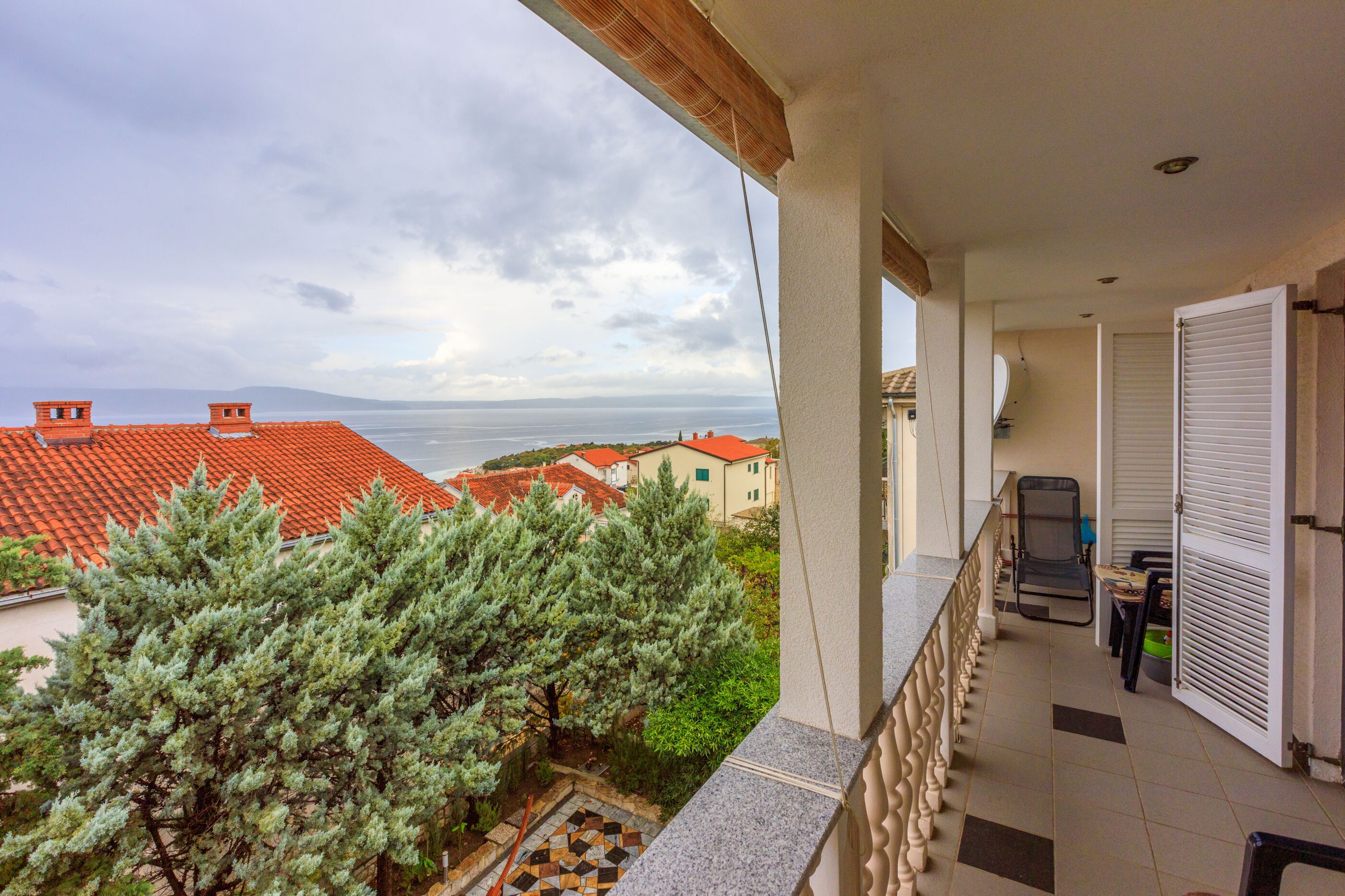 En balkong med utsikt över havet och hus med röda tak.