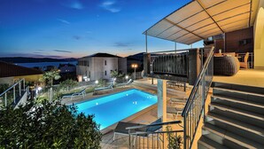 Una piscina con sillas de descanso, una zona de estar techada y una escalera que conduce a un nivel superior.
