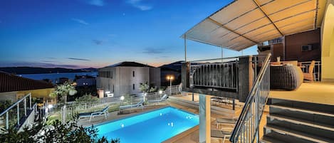 A swimming pool with lounge chairs, a covered seating area, and a staircase leading to an upper level.