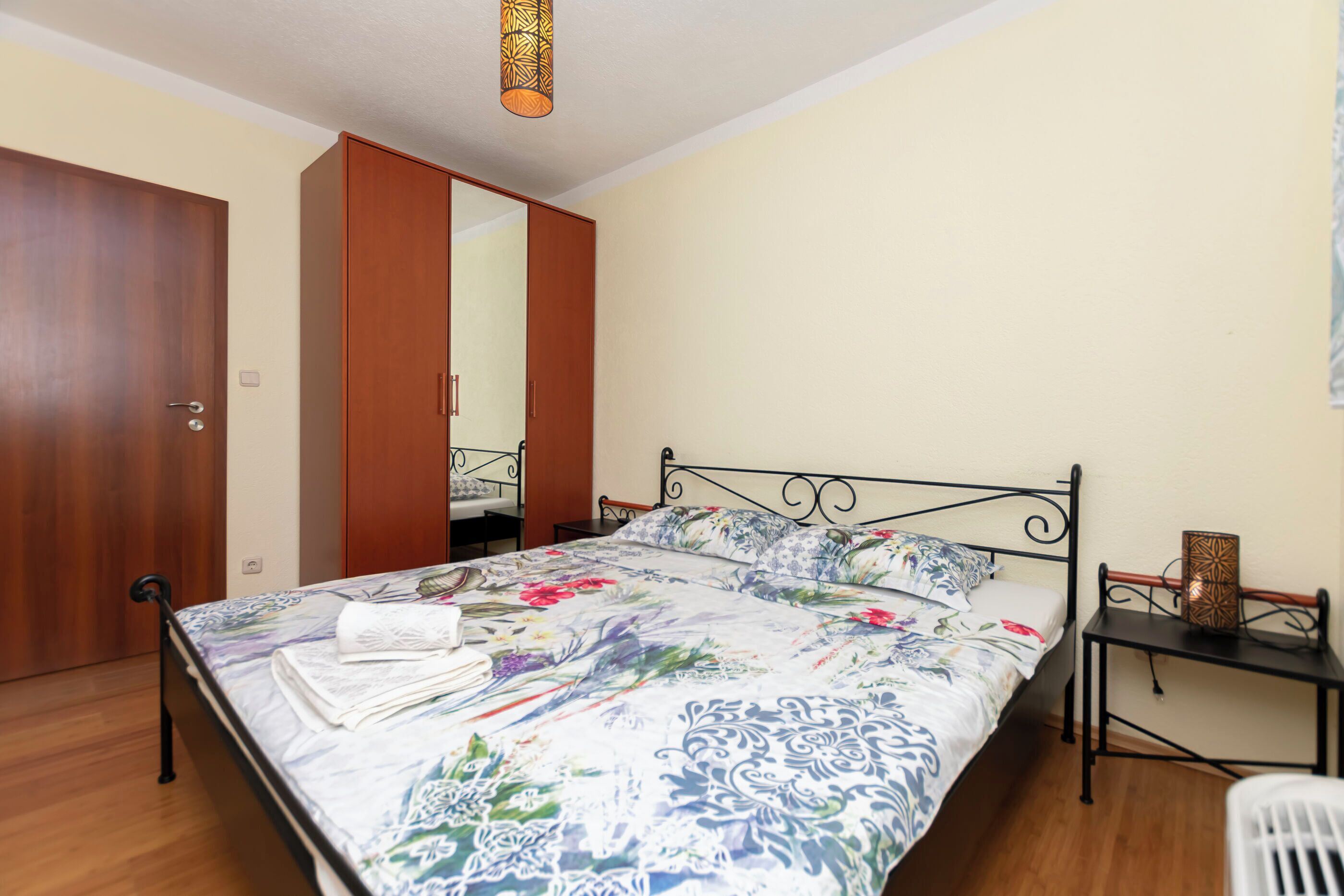 A bedroom with a bed, a wardrobe, a bedside table, and a hanging light fixture.